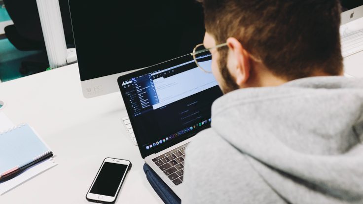 Ein Mann sitzt vor einem Laptop neben dem ein Handy liegt