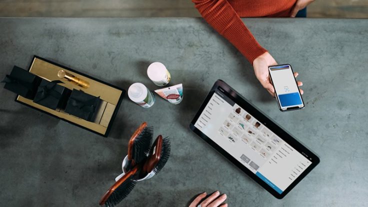 A table with hairbrushes, beauty products and a tablet showing a shopping website