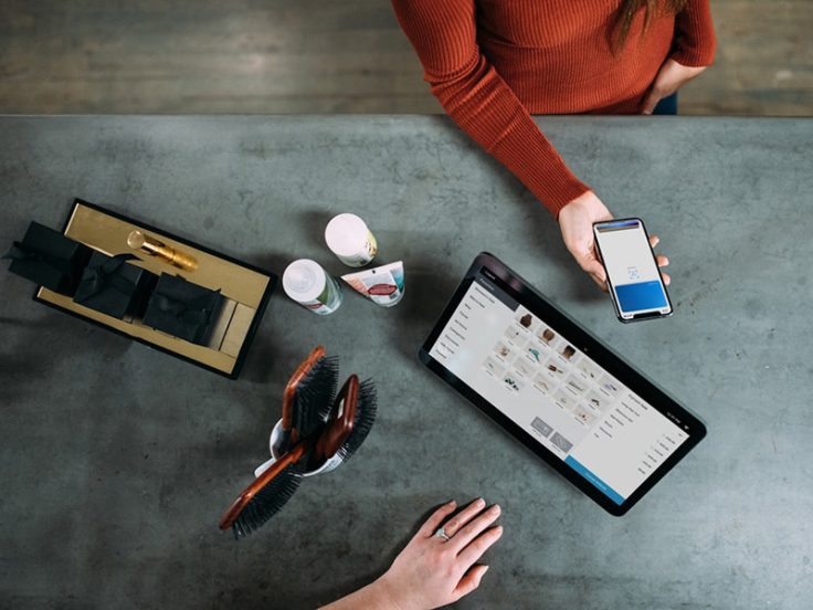 A table with hairbrushes, beauty products and a tablet showing a shopping website