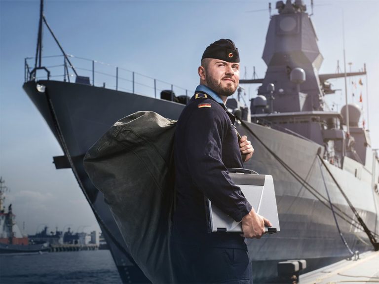 Soldier with Bag and Laptop in his hands, standing in front of a ship