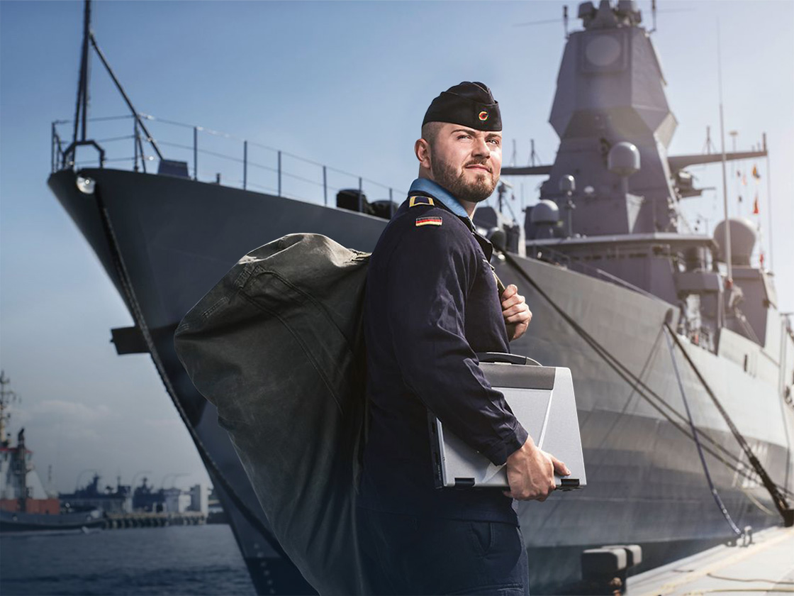 Bundeswehr Soldat mit Laptop und Tasche im Arm vor einem Schiff