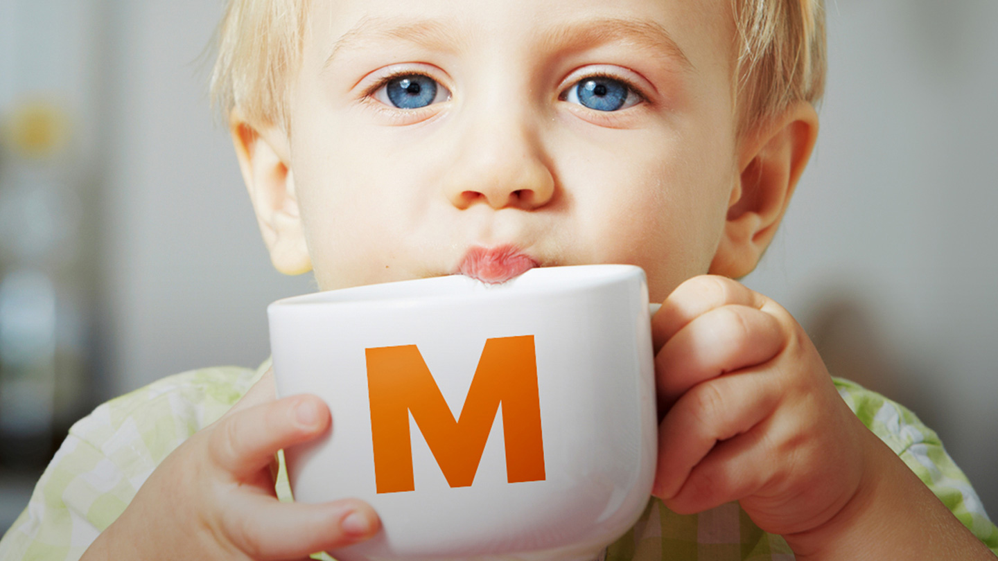 Child drinking from cup with the orange letter M on it.