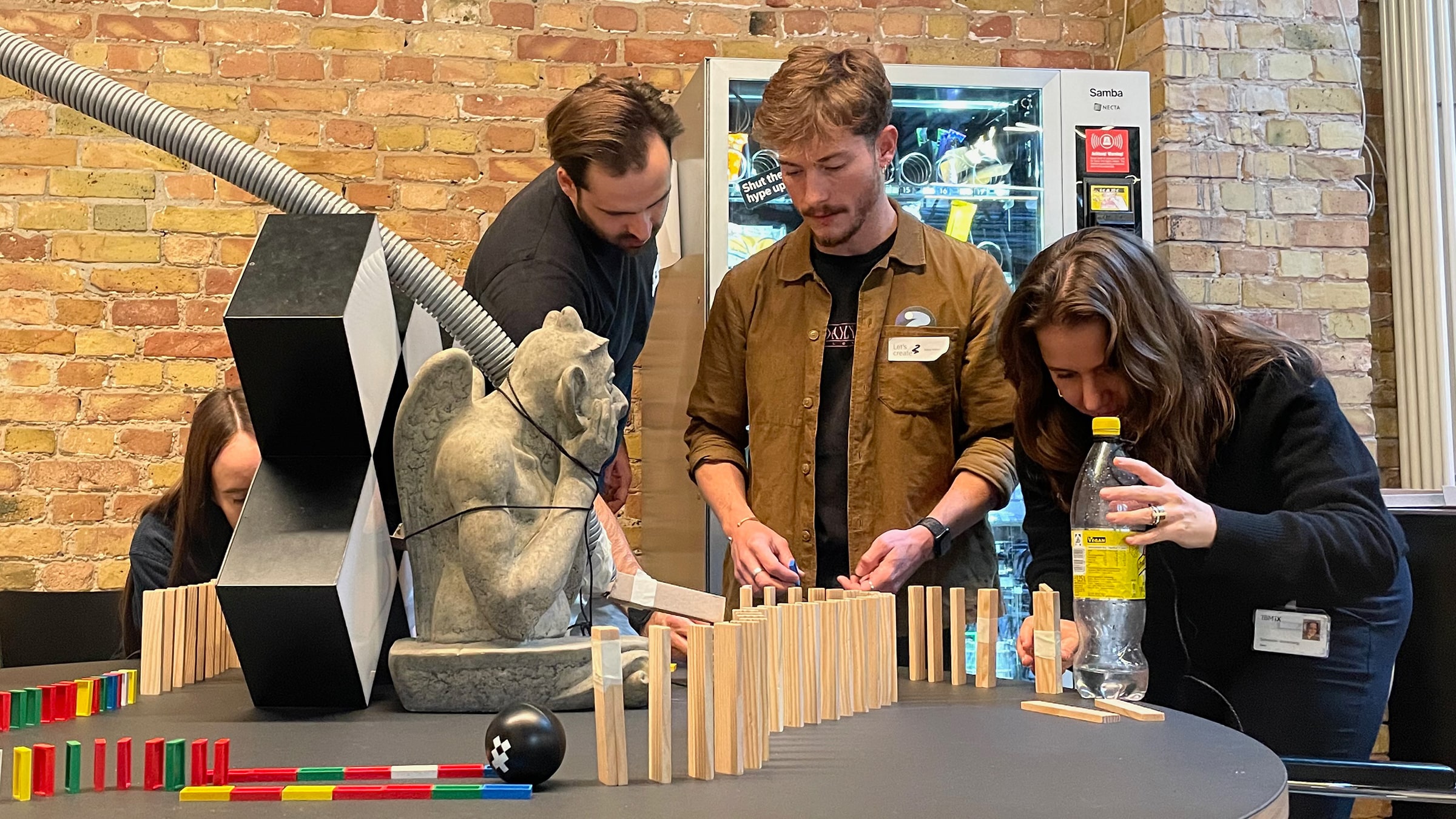 Drei Personen bauen im Büro eine Rube-Goldberg-Maschine