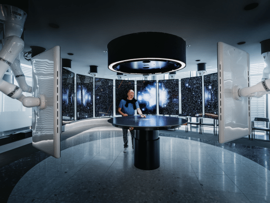 A person in a futuristic control room surrounded by large screens displaying space imagery.